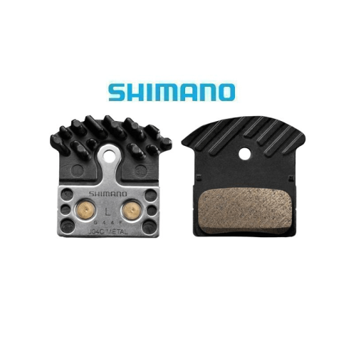 Två Shimano XTR J04C skivbromsbelägg i metall, tydligt fotograferade mot en vit bakgrund. Belysningen framhäver detaljerna i materialen och designen, vilket skapar en ren och informativ bild.