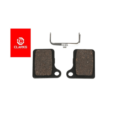 Två organiska skivbromsbelägg från Clarks för Shimano BR-M555, tillsammans med en metallfjäder. Produkterna är placerade mot en vit bakgrund med Clarks logotyp synlig.