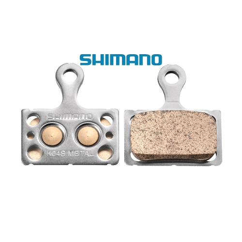Närbild på Shimano K04S metall bromsbelägg för racerbromsar, framställda mot en vit bakgrund. Detaljerade texturer och metallisk glans framhävs i ett jämnt ljus.