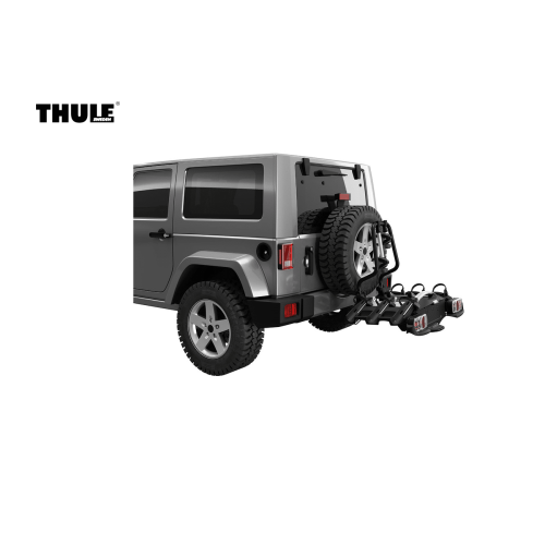 En grå SUV med ett bakmonterat reservhjul har en Thule VeloSpace XT 3-Bike Spare Wheel Adapter monterad på baksidan, som sträcker sig utåt för att rymma två cyklar. Thule-logotypen syns på bildens vänstra sida.