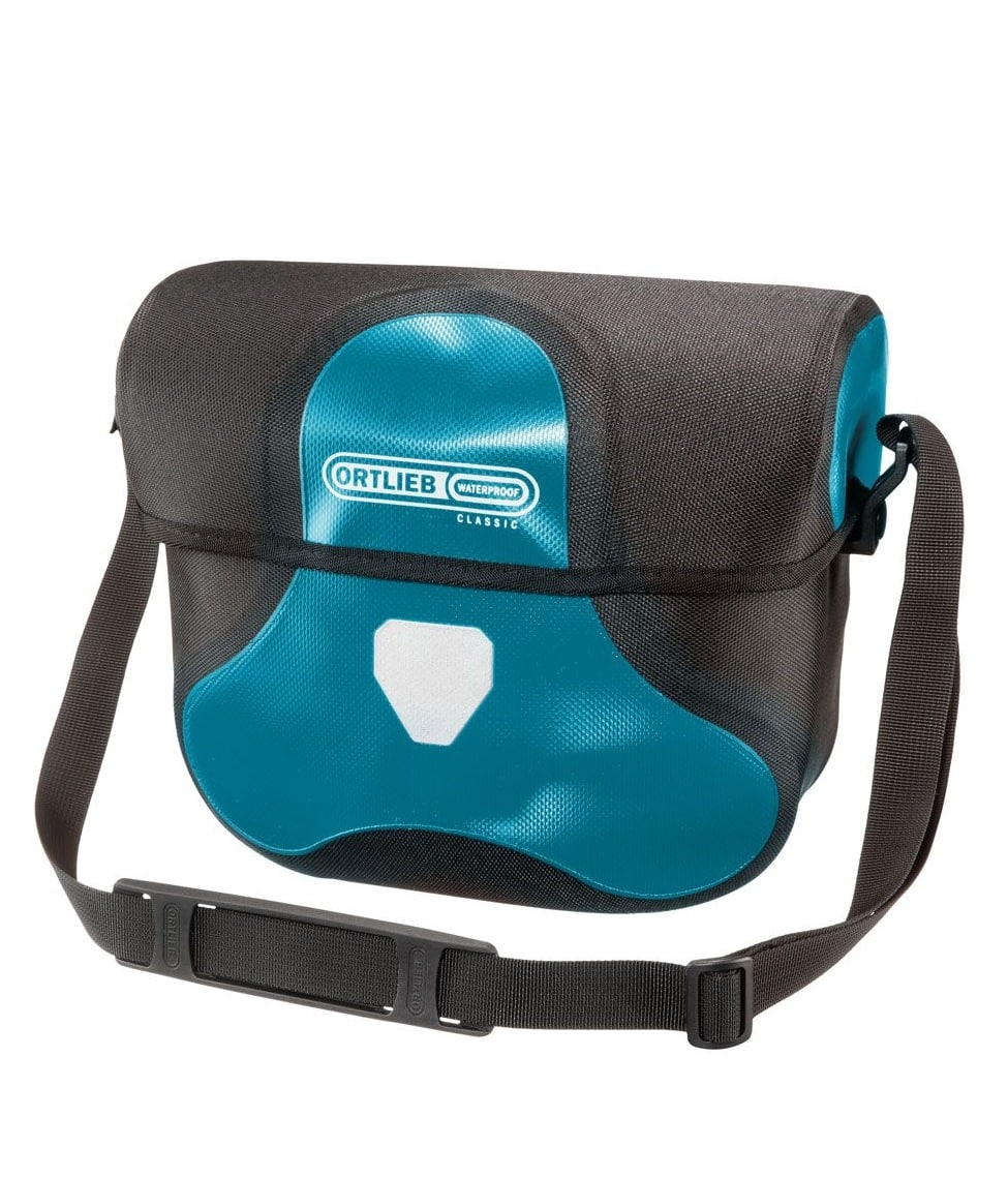 ultimate-six-classic-7l-Petrol.jpg Ortlieb Ultimate Six Classic 7 liter är en blå och svart vattentät axelremsväska med en lång justerbar rem, frontklaff, vit reflekterande patch och visar Ortliebs varumärke med en "Classic"-etikett på framsidan.