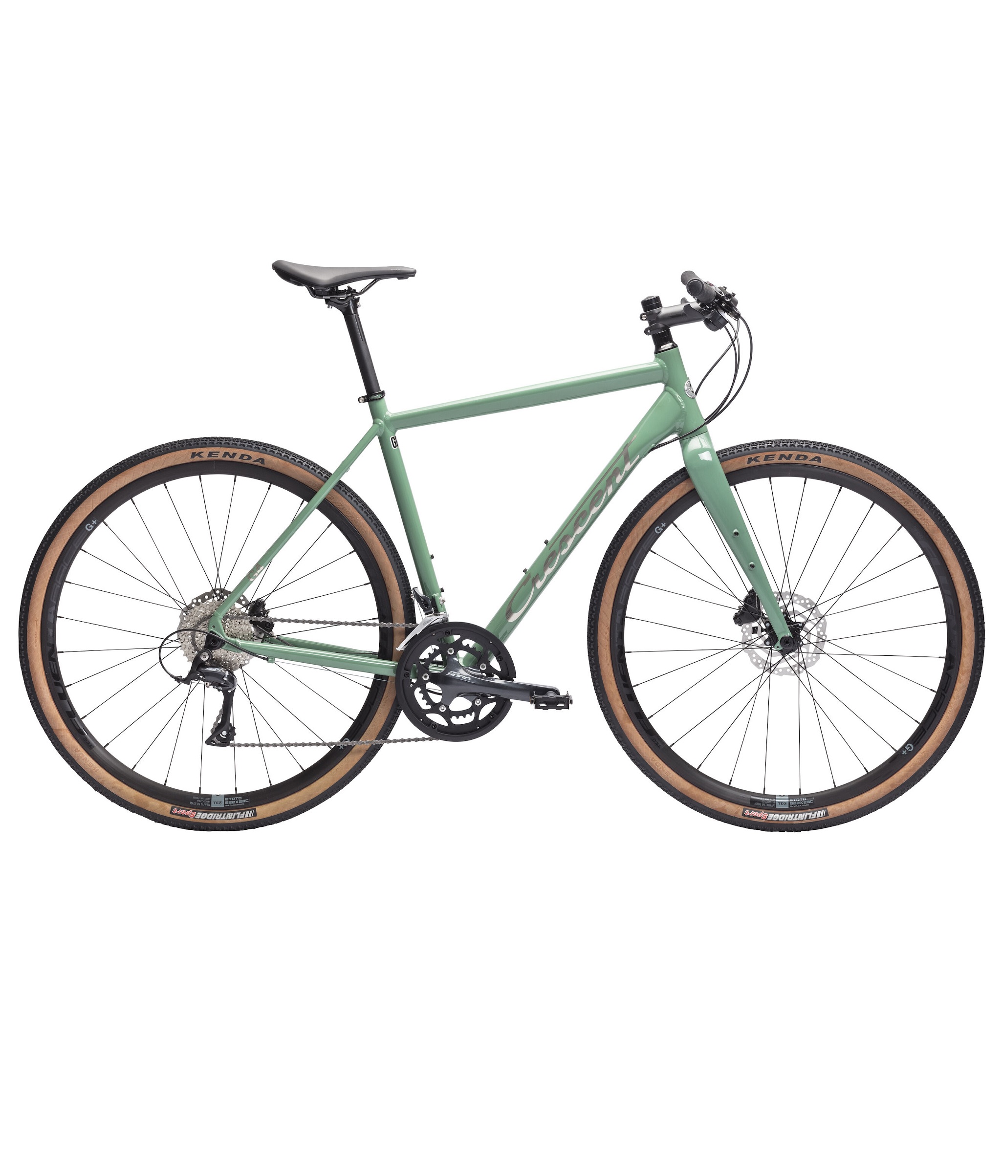 Crescent-Grus-Sport-G4-Green.jpg Grön Crescent Grus Sport G4 gravelcykel i studioljus. Fokus på det breda däcken med "G+" och "KENDA" synligt. Belysningen framhäver cykelns detaljer och den ljusa bakgrunden bidrar till ett rent utseende.