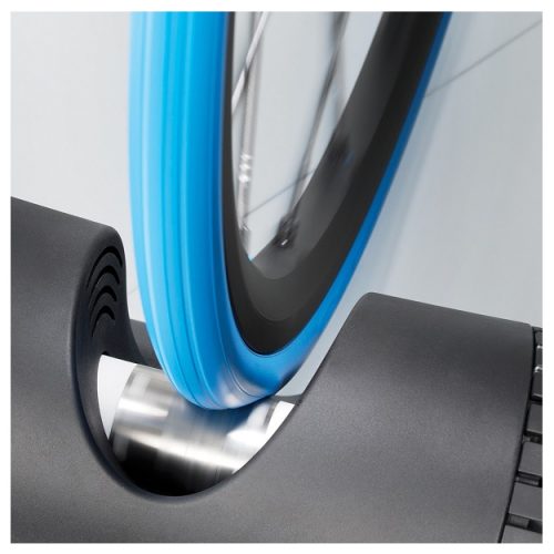 En blått cykeldäck på en Tacx trainer, rullandes mot en silverfärgad rulle. Ljuset reflekteras på rullen, vilket skapar en metallisk glans och en modern känsla.