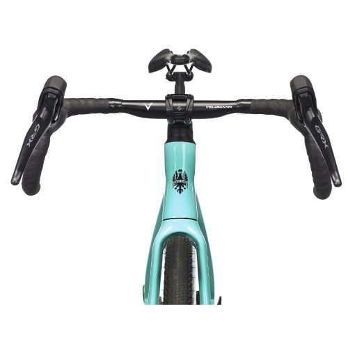 En detaljerad vy av en Bianchi Impulso Comp gravelcykel, fokuserad på styret och den ikoniska celeste-ramen. Marken syns i bakgrunden, allt i skarpt ljus.