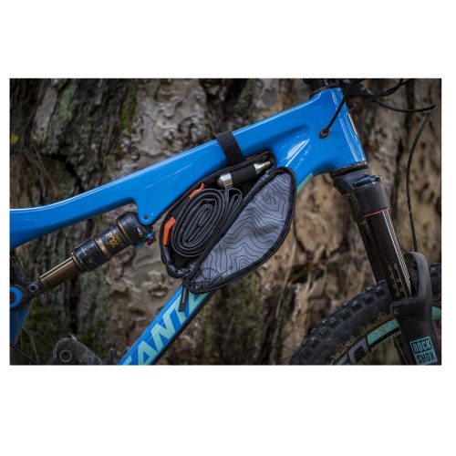 Närbild av en blå mountainbike med en svart Blackburn Outpost Corner-ramväska fäst. Väskan är fylld med en innerslang och en kolsyrepatron, och bakgrunden visar en skogsmiljö i dämpad belysning.