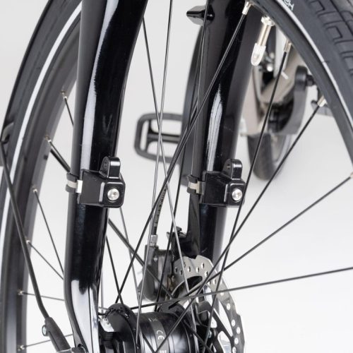 Närbild av ett svart cykelhjul med skärm och navgenerator, framgaffel med två fästen för pakethållare. Fokus ligger på detaljerna och den släta bakgrunden ger bra kontrast.