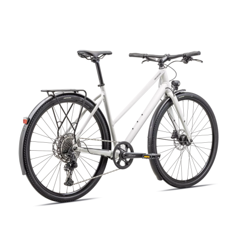 En ljusgrå Specialized Sirrus X 3.0 EQ ST Disc hybridcykel i profil mot en vit bakgrund. Cykeln har skärmar, pakethållare och framlampa, vilket indikerar dess praktiska användning.