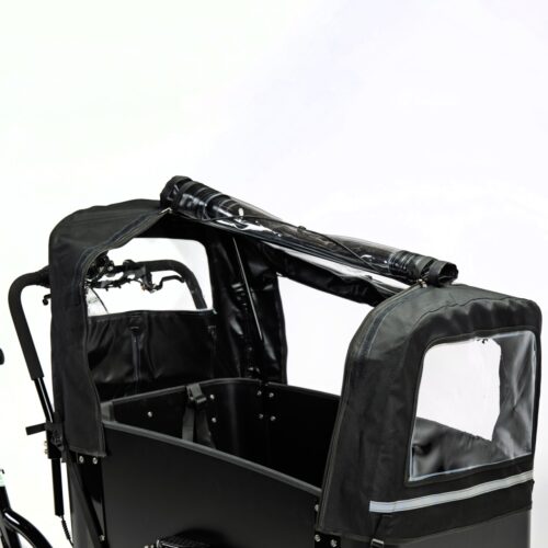 En närbild av Lastcykel Cargobike Delight, en svart lastcykel utrustad med ett regnskydd med genomskinliga plastfönster och en upprullad övre del, fotograferad mot en enfärgad vit bakgrund.