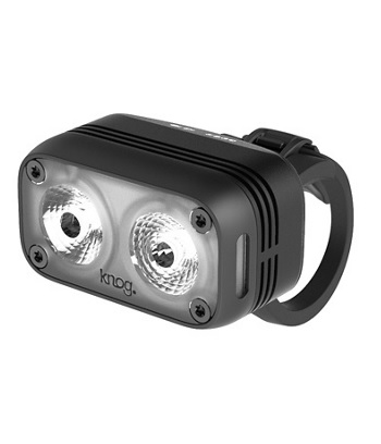 Närbild av Knog Blinder Road 400 lumen framlampa. Den mattsvarta lampan har två lysdioder, fästrem och synliga skruvar. Starkt ljus reflekteras från linserna, mot en ljus bakgrund.