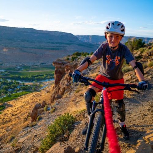 Pojke på mountainbike, bergslandskap i bakgrunden. Varmt ljus förstärker den äventyrliga stämningen. Pojken bär skyddsutrustning och cykeln är utrustad med Bogserlina TowWhee.