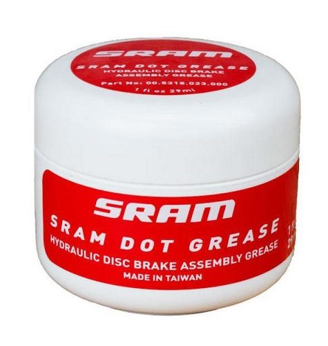 En burk SRAM DOT-fett för bromsok står i fokus, med röda och vita etiketter. En ren, studioliknande miljö framhäver produktens detaljer och text.