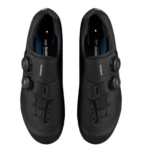 Två svarta Shimano SH-RC703 landsvägsskor visas ovanifrån. Skorna har ett modernt utseende med BOA-spännen och perforerade detaljer, presenterade i ett väl upplyst och professionellt foto.