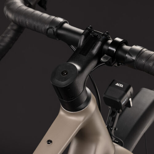 Närbild på en Gravel Cube Nuroad ONE FE 1x9s – Bruns styre, styrstam och främre ramdel mot en svart bakgrund. Cykeln har lindade handtag, integrerade kablar och en elektronisk växlingsenhet monterad nära styret.