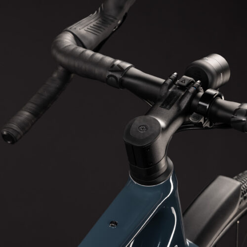 Närbild på Gravel Cube Nuroad Race FE, 2x12s – Blå cykelns styre, styrstam och främre ramdel. Styret, som är lindat med svart tejp, och den mörkblå ramen sticker ut mot den helt svarta bakgrunden och lyfter fram de högkvalitativa komponenterna i Gravel Cube Nuroad Race FE.
