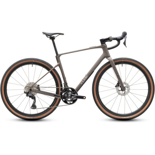 En mattbrun Cube Nuroad C:62 Pro-gravelcykel (2x12-växlad) med drop-styre, två flaskhållare, breda däck med bruna sidoväggar, skivbromsar och en drivlina med dubbla kedjedrev. Cykeln visas i sidoprofil mot en vit bakgrund.