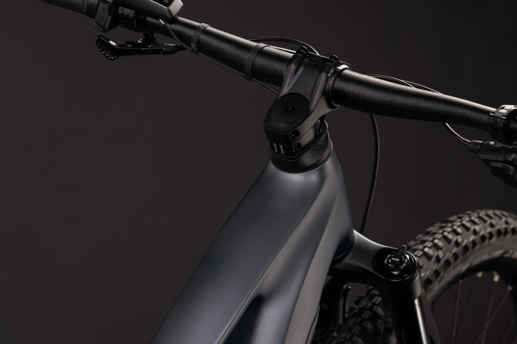 Närbild på El-MTB Cube Stereo Hybrid ONE22 PRO 800 – Grås mattsvarta styre, styrstam och främre ramdel mot en enfärgad mörk bakgrund, med en delvis vy av den främre fjädringsgaffeln och mönstret på framdäcket.