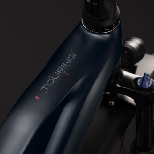 Närbild av en mörkblå EL-cykel av modellen Cube Touring Hybrid ONE 600 Trapeze – Svart, där orden ”TOURING” och ”ONE” syns tryckta på överröret, med en del av framgaffeln och däcket synliga mot en svart bakgrund.