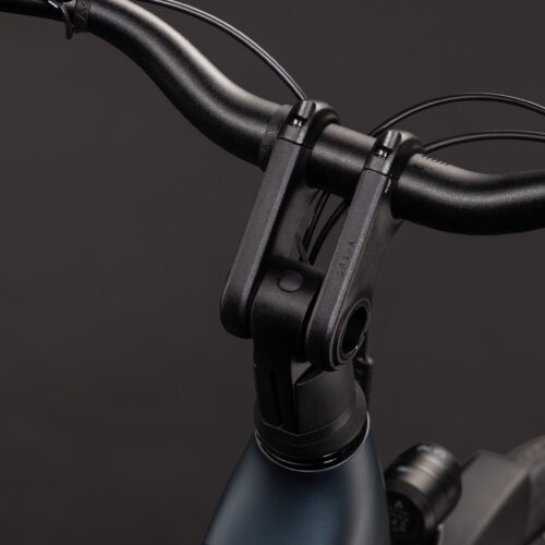 Närbild på styret och styrstammen på EL-cykel Cube Supreme RT Hybrid Comfort EX 600, Fotbroms – Blå/grön mot en enfärgad mörk bakgrund, där cykelramens främre del, bromskablarna och framhjulets ovansida syns.