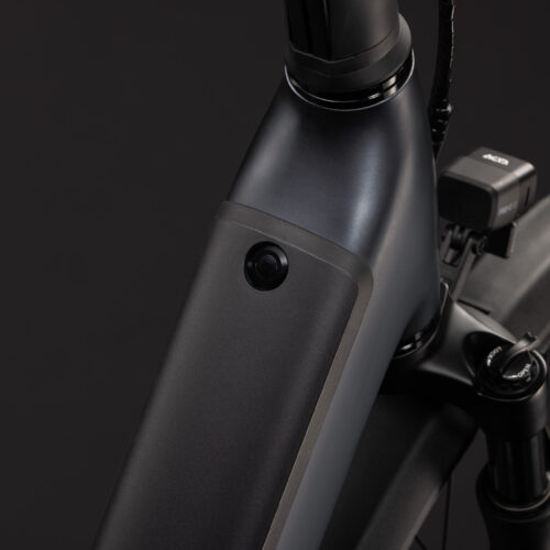 Närbild på EL-cykeln Cube Supreme Hybrid Pro 6600 med lågt insteg i svart, där ramen har en inbyggd strålkastare, en framgaffel med fjädring och en elektronisk display monterad på styret. Den mörka bakgrunden framhäver cykelns detaljer.