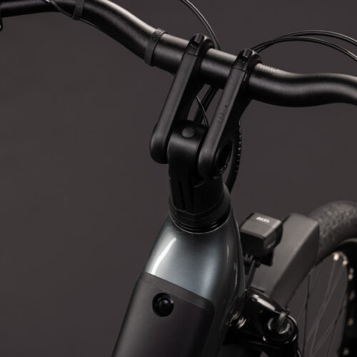 Närbild på styret, styrstammen och framhjulet på EL-cykel Cube Supreme RT Hybrid Deluxe EX 600, där den eleganta silvermetallic-ramen och de synliga bromskablarna framträder tydligt mot en mörk bakgrund.