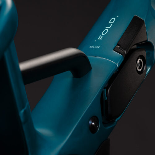 Närbild på ramen till en blå EL-cykel av modellen Cube Fold Hybrid Delu545, där den eleganta ”Fold Deluxe”-etiketten och den karakteristiska svarta låsmekanismen syns tydligt. Den mörka bakgrunden framhäver ramens släta yta och designelement, med subtila detaljer som antyder den innovativa Fold Hybrid-konstruktionen.