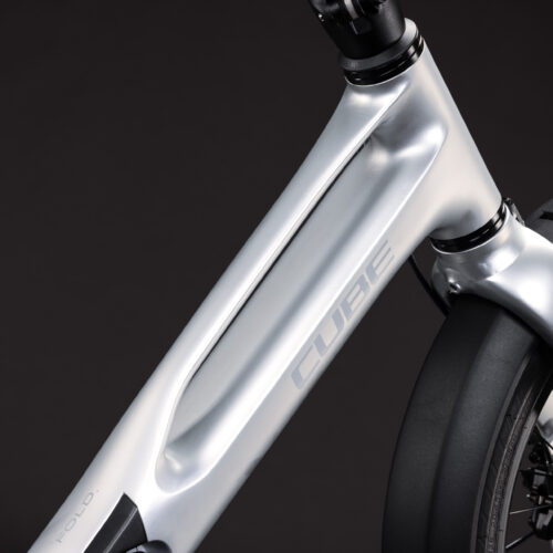 Närbild på den metalliskt silverfärgade ramen till EL-cykel Cube Fold Hybrid 540, med ”CUBE”-logotypen på sidan. Bilden visar även en del av framhjulet, stänkskärmen och skivbromsen mot en mörk bakgrund.