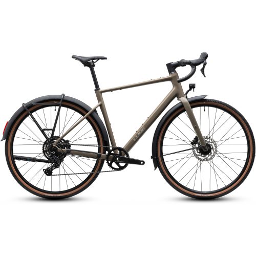 En mattbeige gruscykel med drop-styre, skivbromsar, skärmar fram och bak samt däck med bruna kanter, avbildad i profil mot en vit bakgrund. Cykeln har ett lutande överrör och infällda kablar.