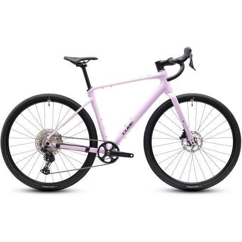 En ljusrosa gruscykel med drop-styre, skivbromsar, en svart sadel och två stora däck visas i profil mot en vit bakgrund. Cykeln har ett enda kedjehjul fram och en synlig kuggkassett.
