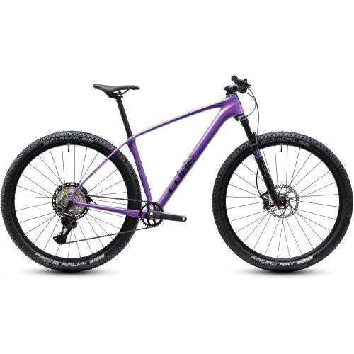 En lila hardtail-mountainbike med kolfiberram, rakt styre, framgaffel med fjädring, skivbromsar och 29-tums hjul. Däcken är märkta med ”Schwalbe Racing Ralph”. Cykeln är fotograferad från sidan.